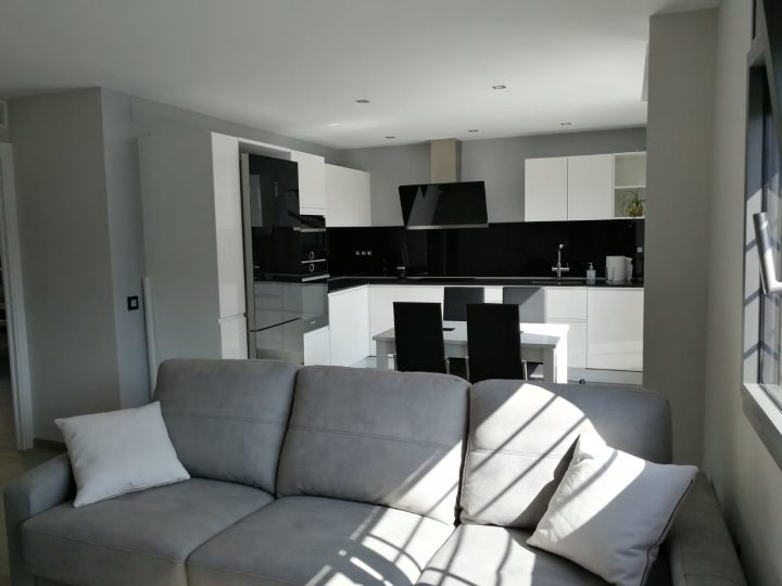 Cocina después de la reforma: cocina abierta al salón con muebles blancos y frontal negro